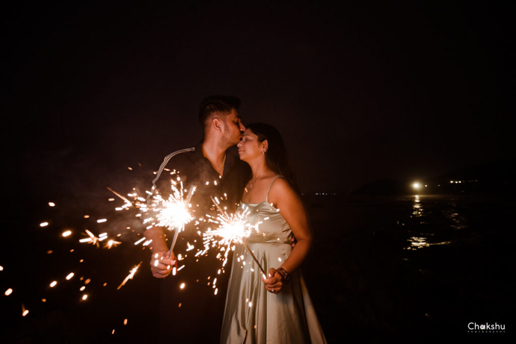 a cute couple standing in front of a beach and handle a fire work image captured by best pre- weeding photographer in delhi.