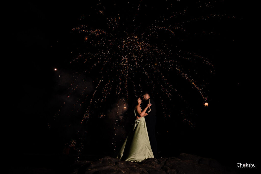 A cute couple standing on a rock in night with fire work in sky image captured by best pre- weeding photographer in delhi.