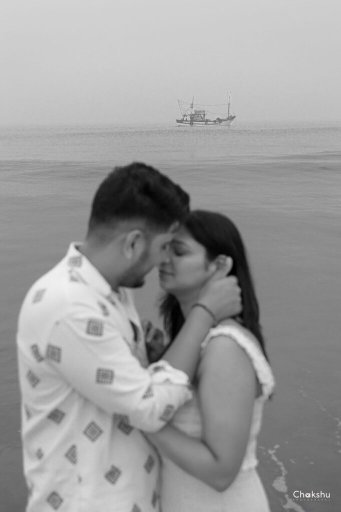 A couple shares a kiss on the beach, with a boat in the background, captured by a pre-wedding photographer in Delhi.